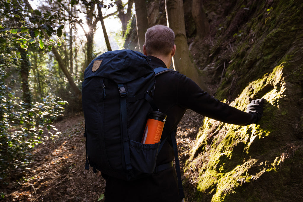 Person with a backpack touching a tree in a forest