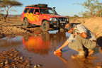Person crouching by a puddle with a red off-road vehicle in the background