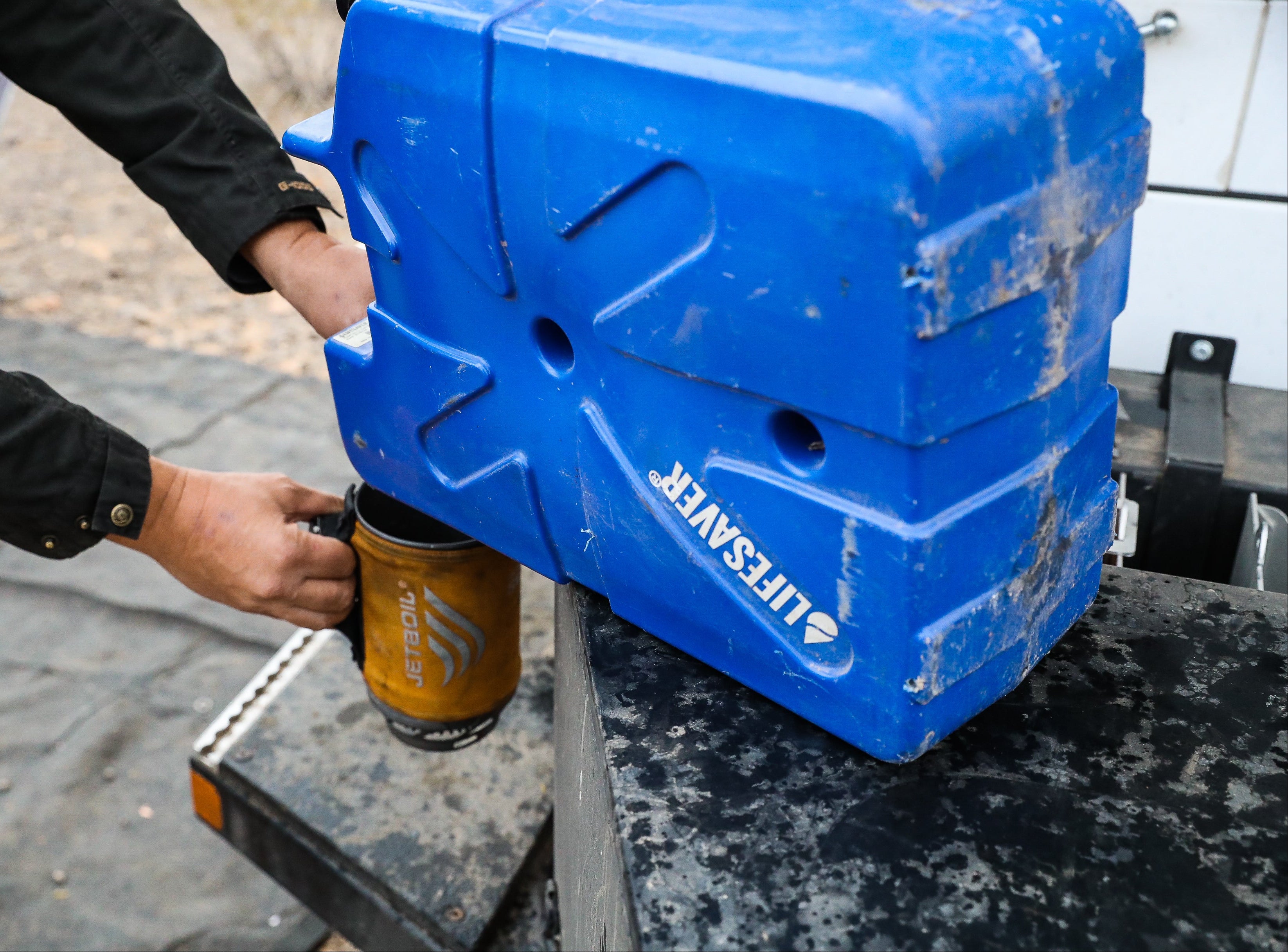 Blue LifeSaver Jerrycan filling a tin cup with purified water