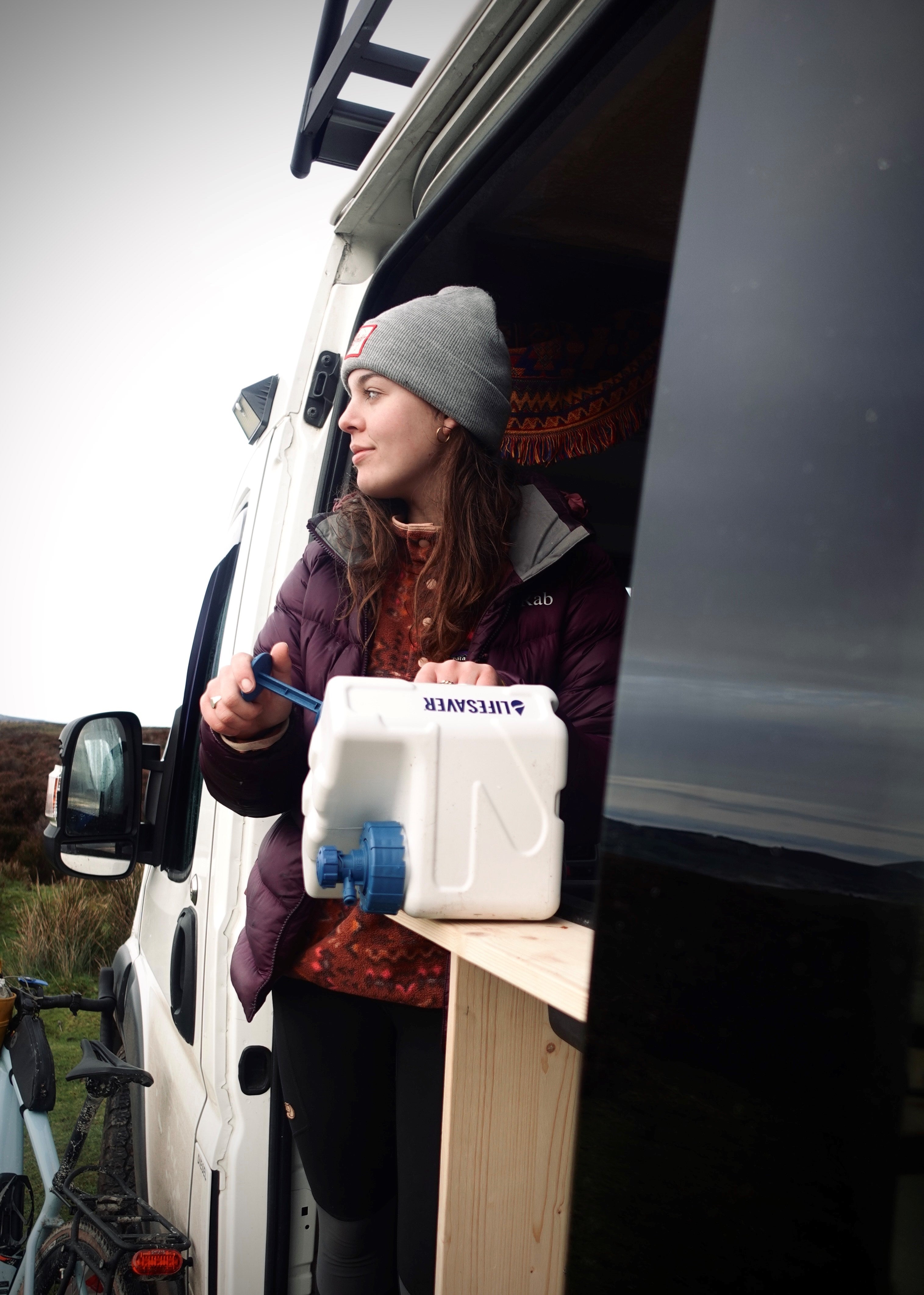 Person standing next to a van with a Cube, wearing a beanie and purple jacket.