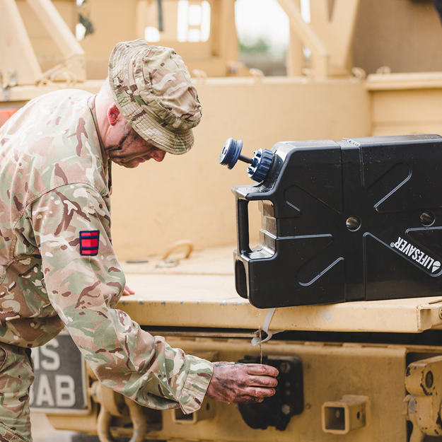 Soldier in camouflage uniform filling a cup from a black LifeSaver Jerrycan on a military vehicle